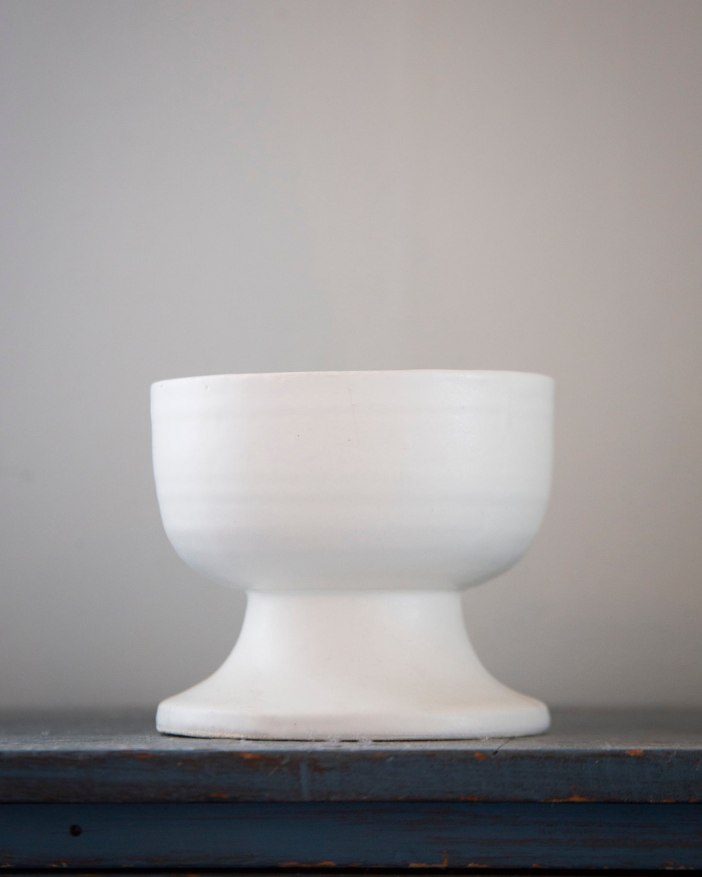 White ceramic footed bowl on a dark surface with a gray background