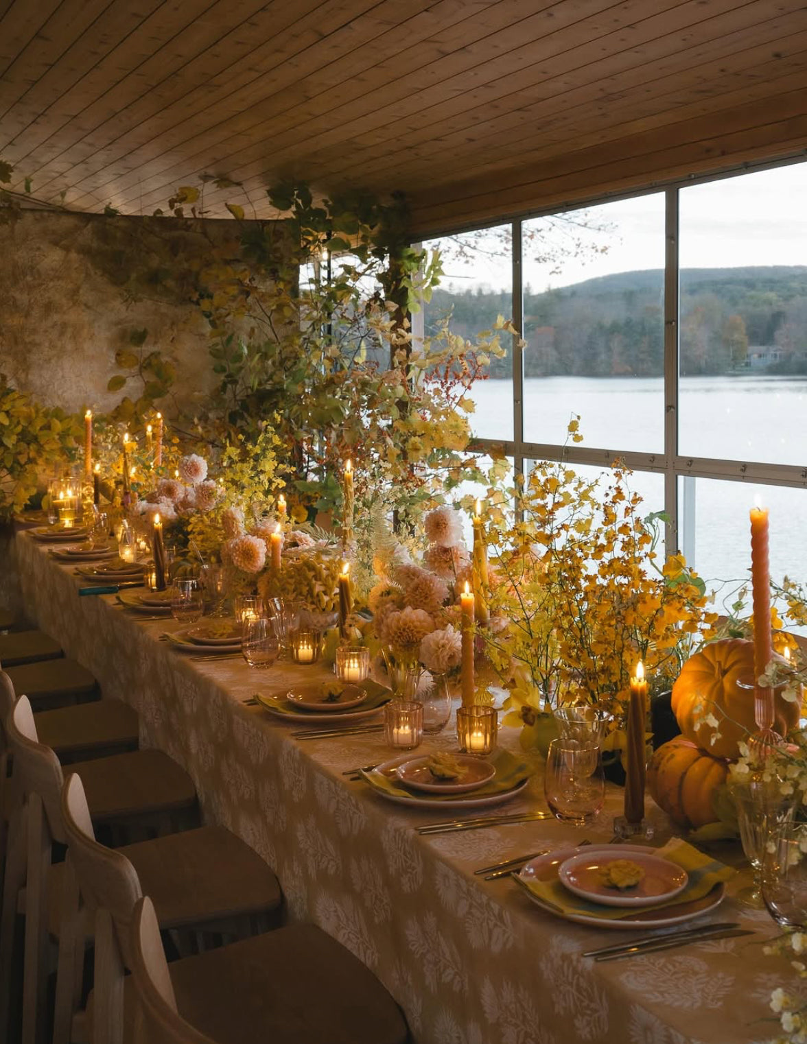 Ariella Chezar and Anne Long Floral Retreat at The Dahlia House in Skagit Valley WA. Dining table set for a meal with candles and flowers, overlooking a scenic view of a lake.
