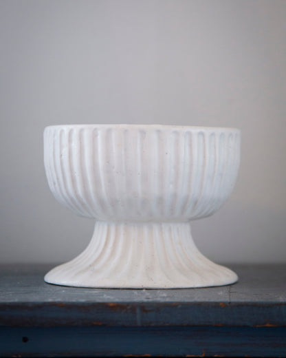 White textured pedestal bowl on a gray surface with a gray background