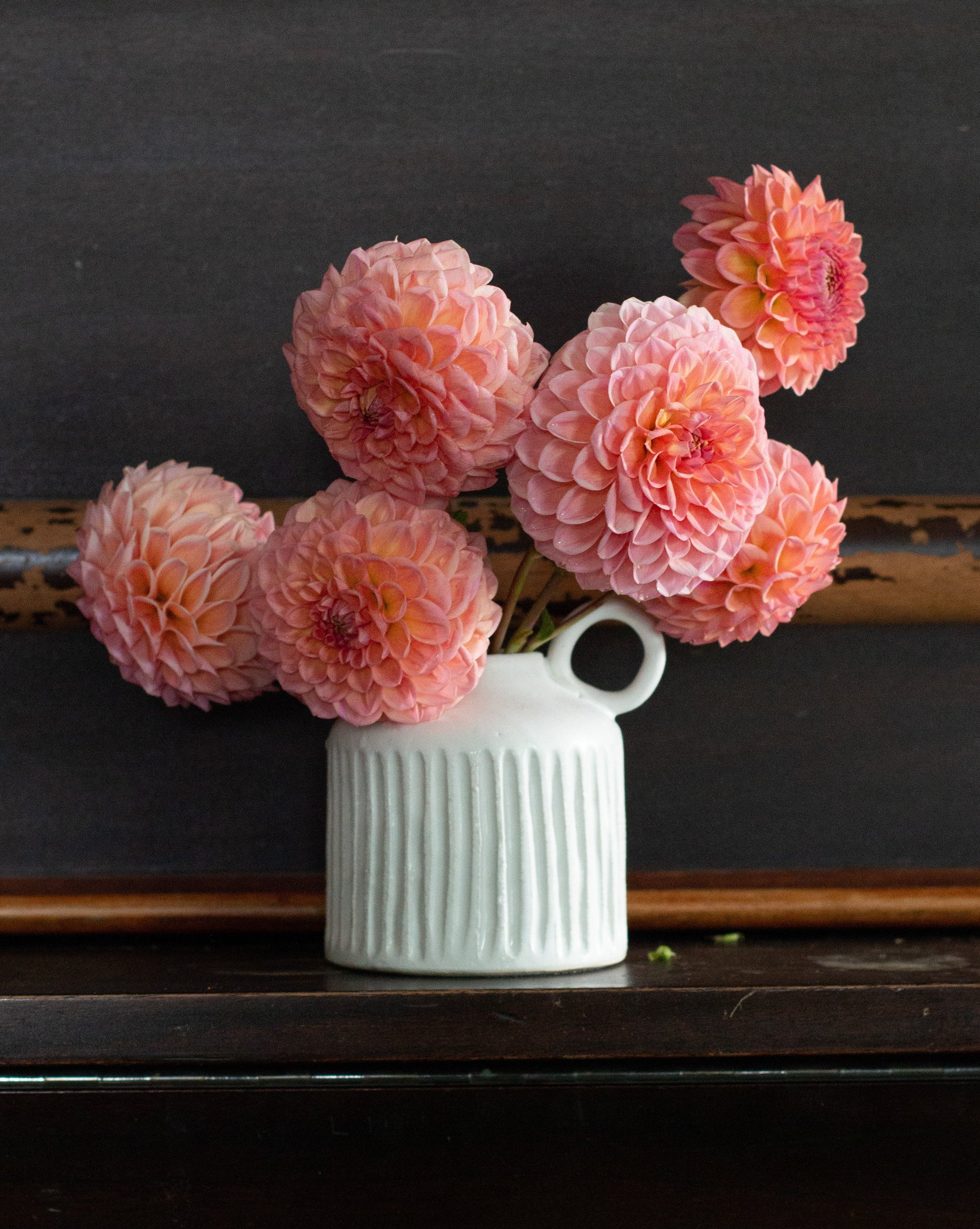 White vase with pink flowers on a dark surface