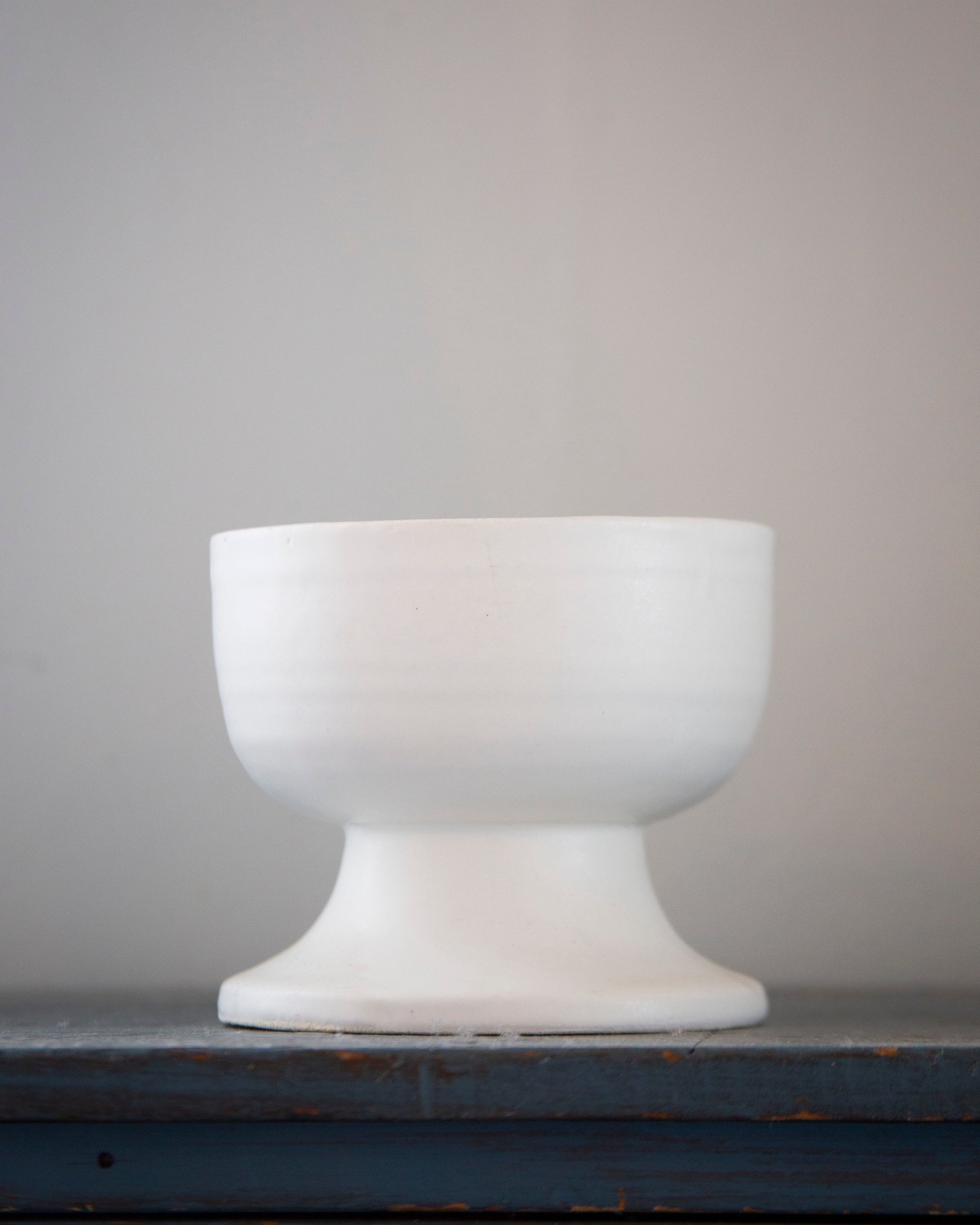 White ceramic footed bowl on a dark surface with a gray background