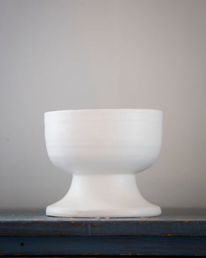 White ceramic footed bowl on a dark surface with a gray background