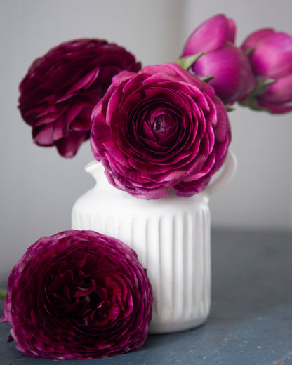 White vase with purple flowers on a gray surface