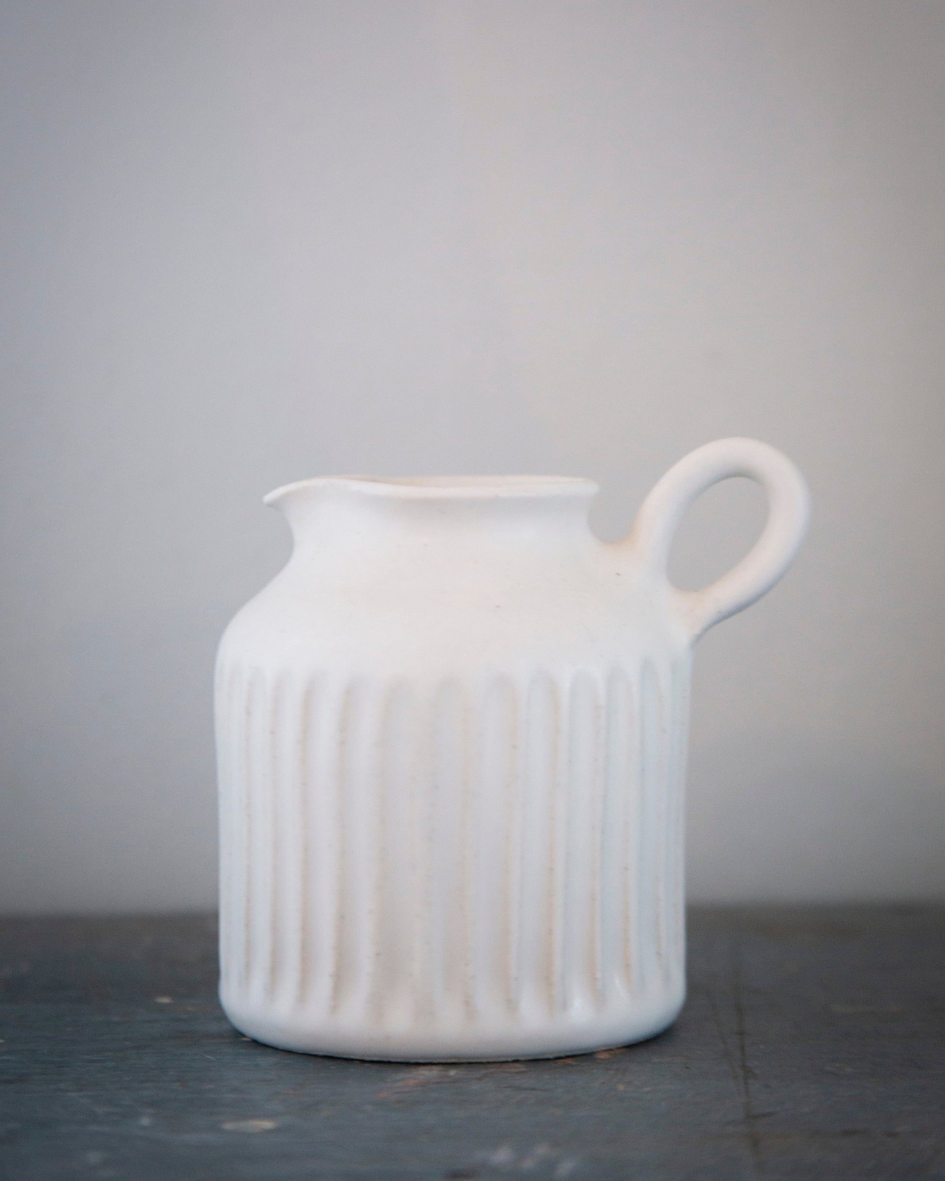 White ceramic pitcher on a dark surface with a light gray background