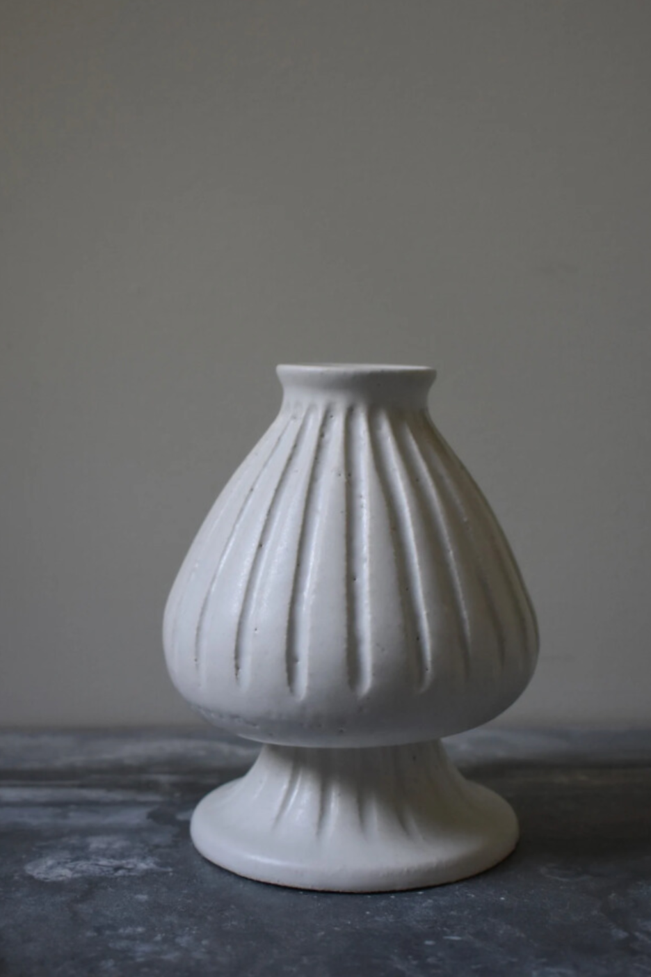 A white, carved ceramic vase with a geometric pattern on the exterior, placed against a neutral background.