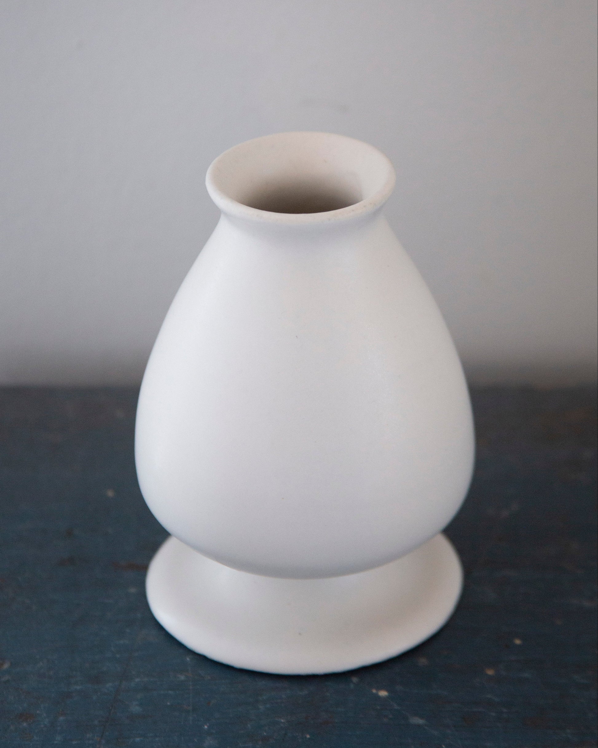 White ceramic vase on a dark surface with a gray background