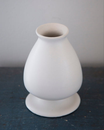 White ceramic vase on a dark surface with a gray background