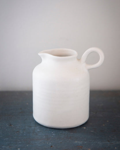 White ceramic pitcher on a dark surface with a light gray background