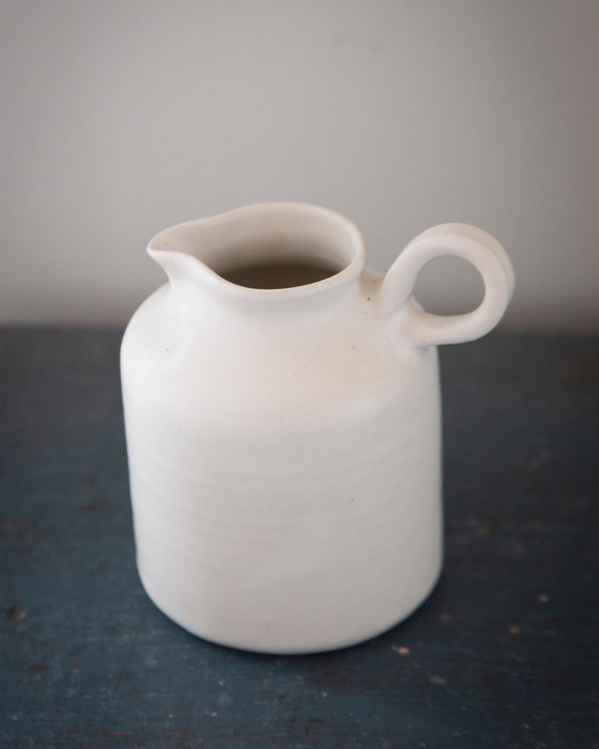 White ceramic pitcher on a dark surface with a gray background