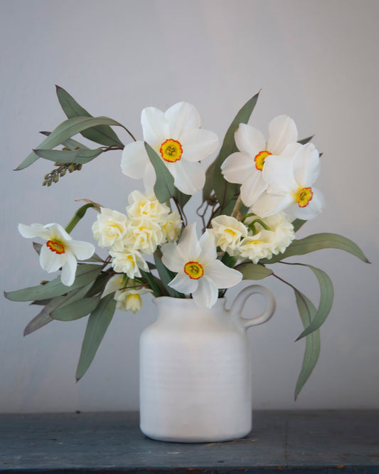 White vase with flowers on a gray surface against a light gray background