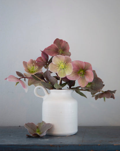 White vase with pink and green flowers on a wooden surface against a light gray background