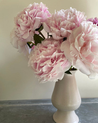 Pink peonies in a white vase on a neutral background