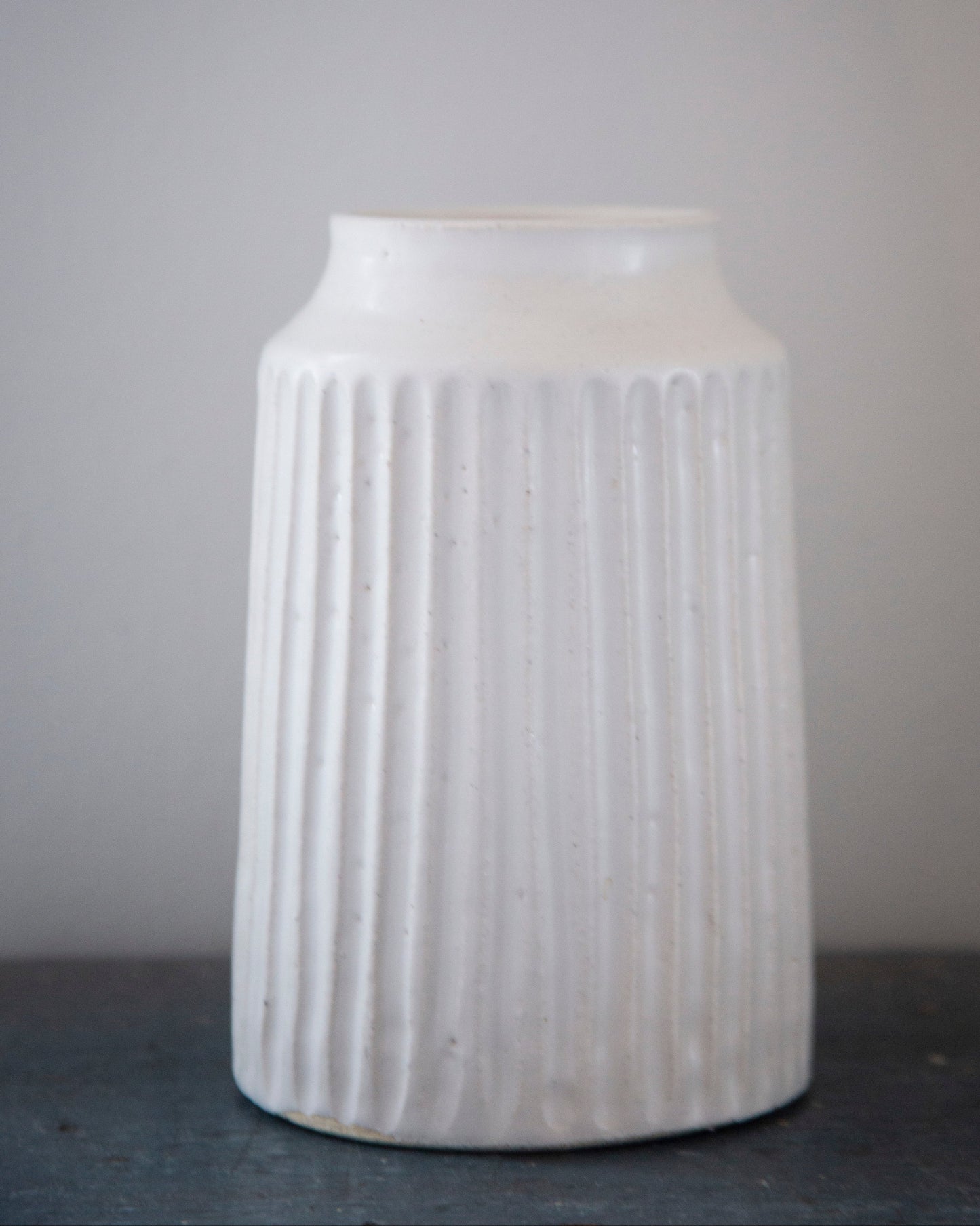 White ribbed ceramic vase on a dark surface with a gray background