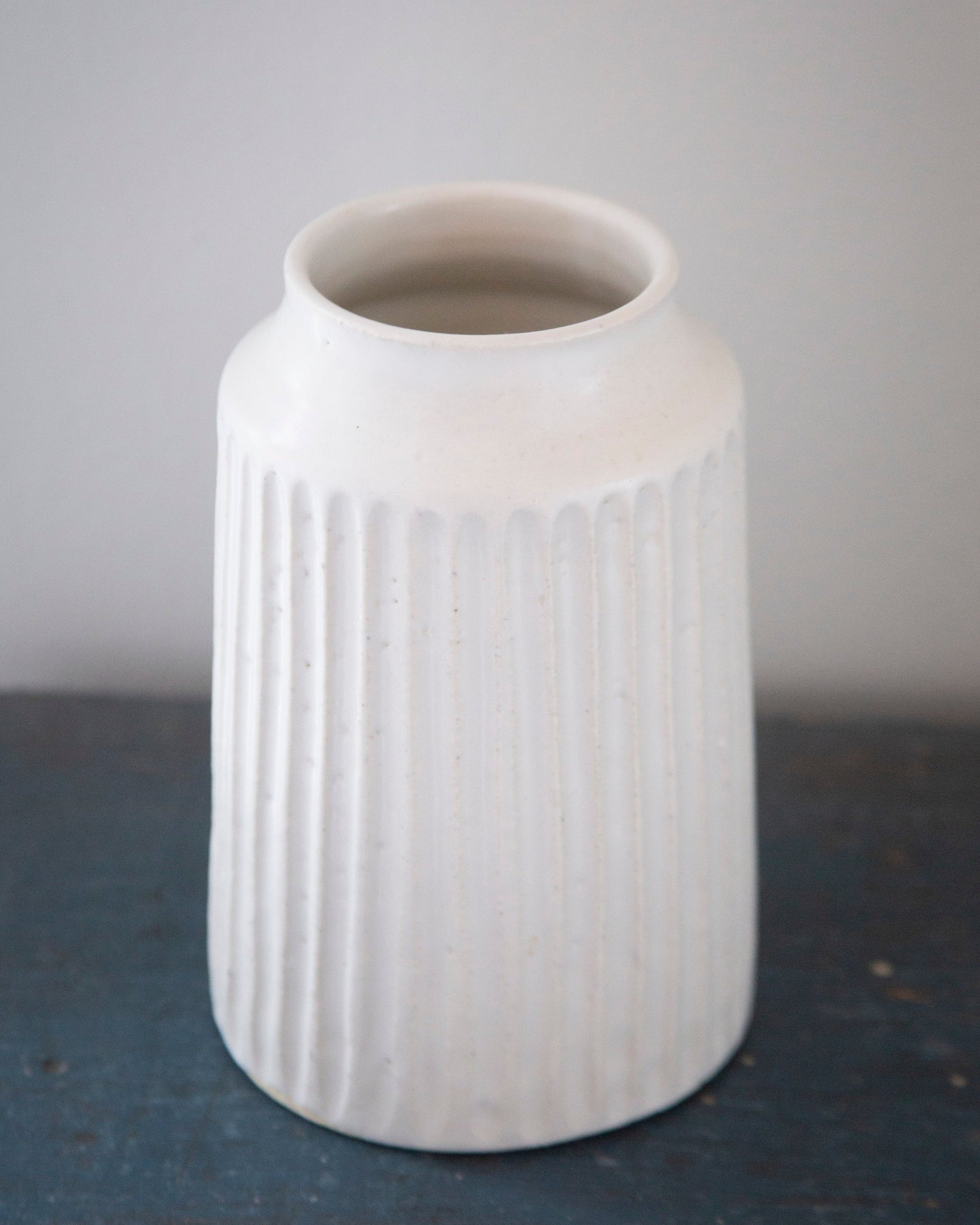 White textured vase on a dark surface with a light gray background