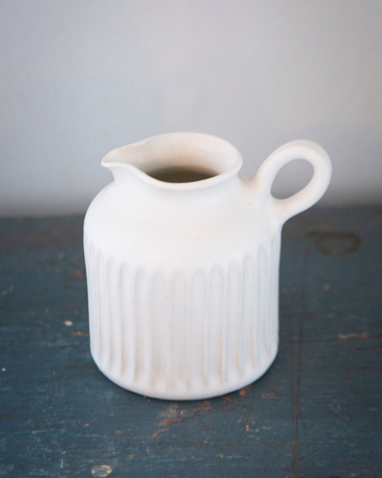 White ceramic pitcher on a dark surface with a gray background