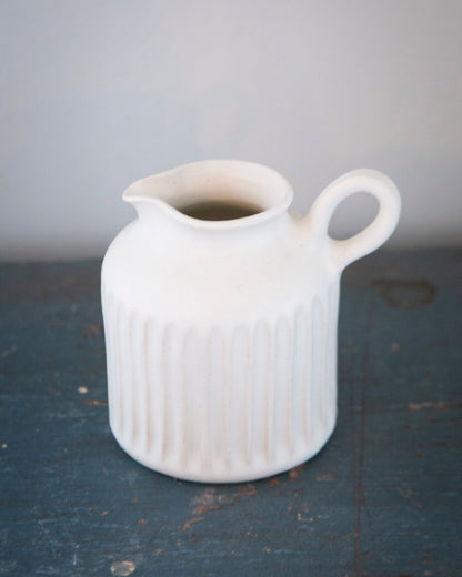 White ceramic pitcher on a dark surface with a gray background