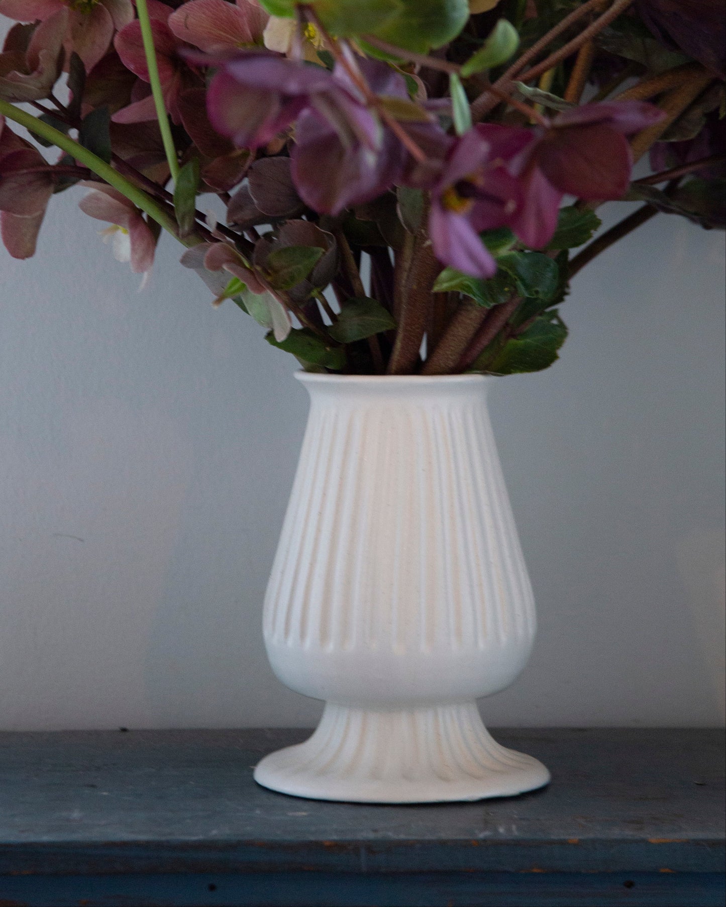 White vase with purple flowers on a wooden surface