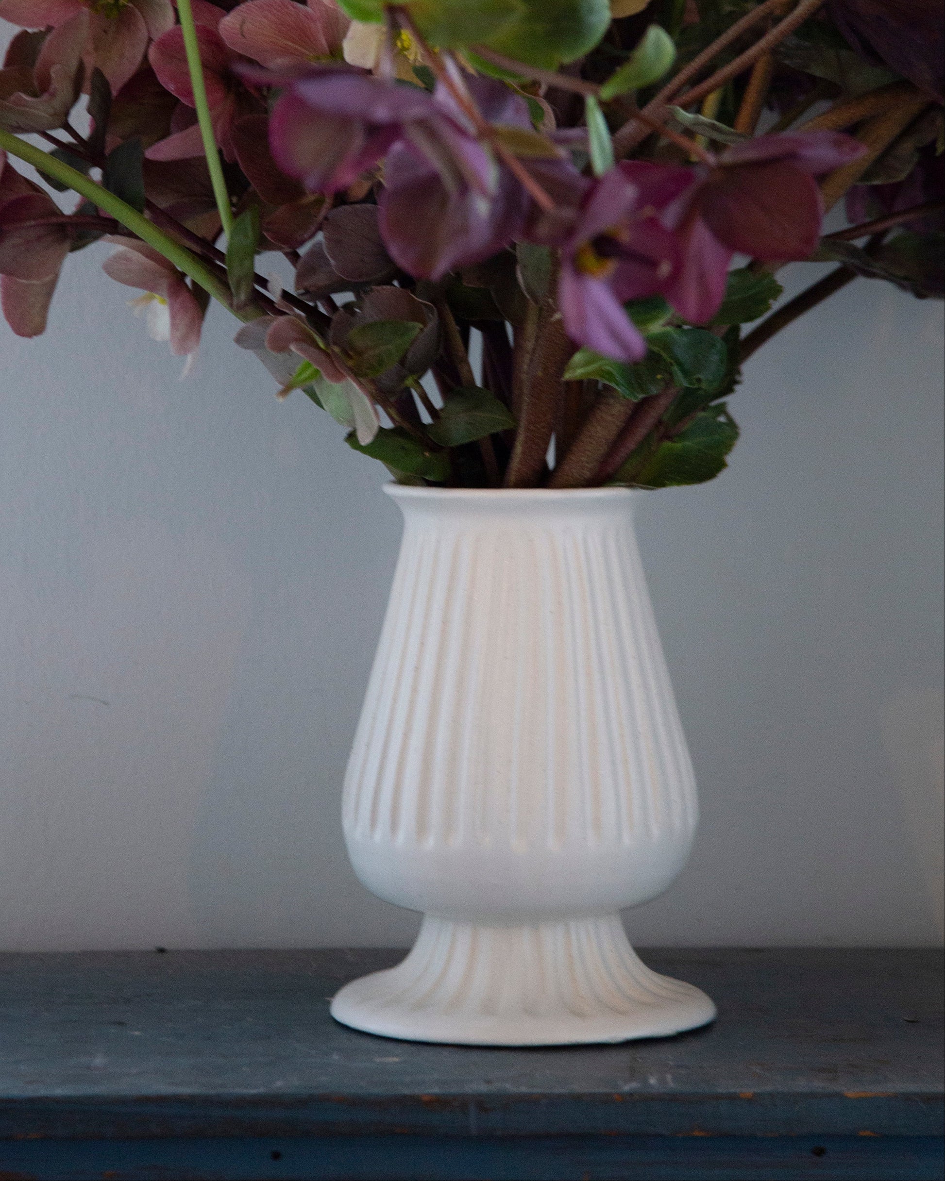 White vase with purple flowers on a wooden surface