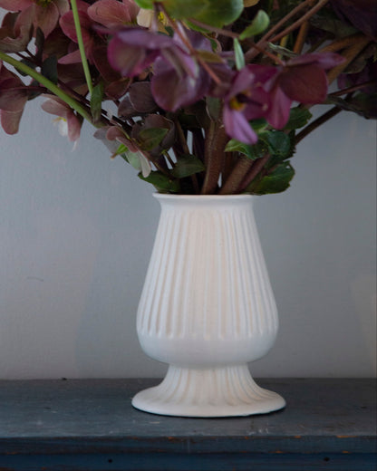 White vase with purple flowers on a wooden surface