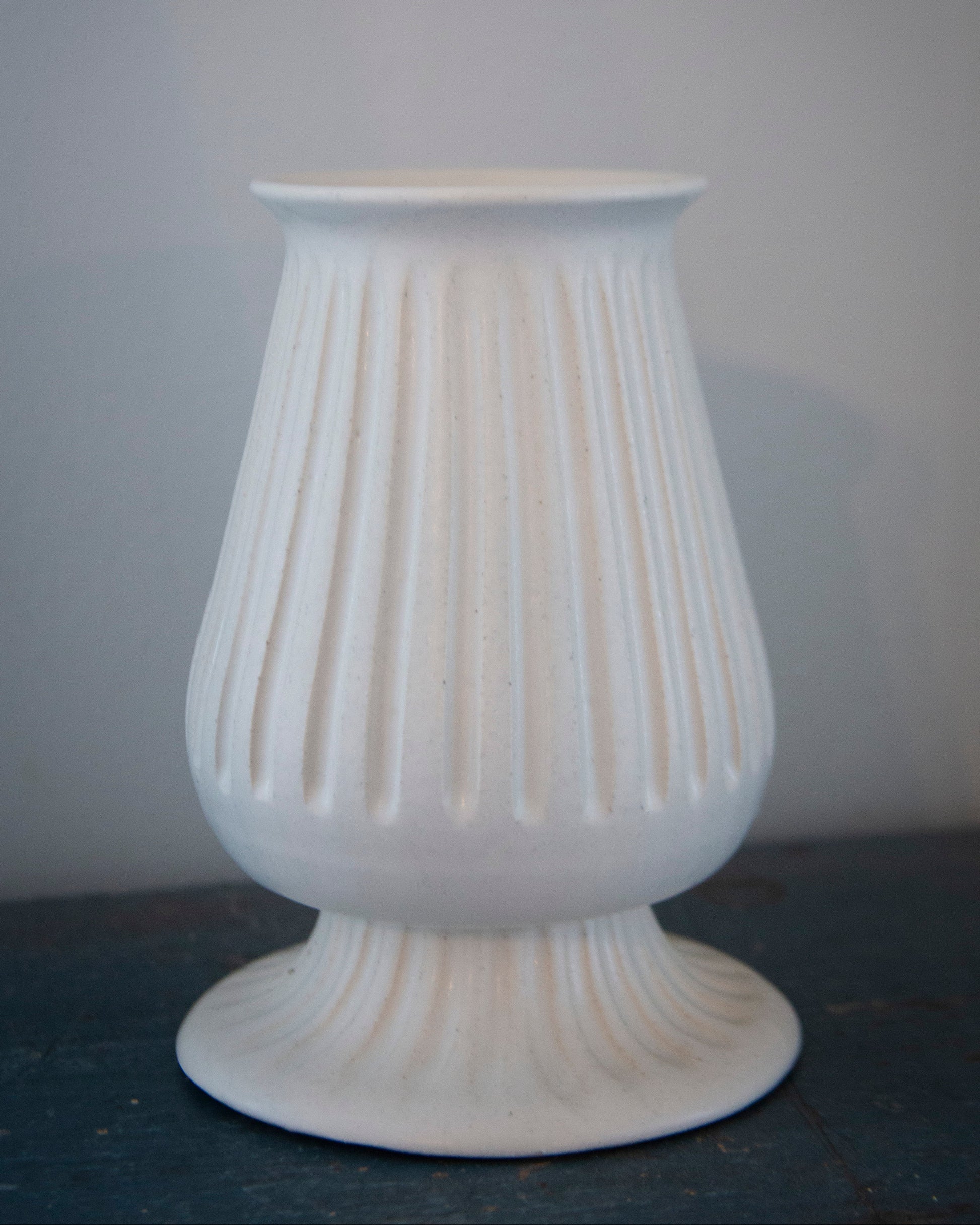 White textured vase on a dark surface with a light gray background