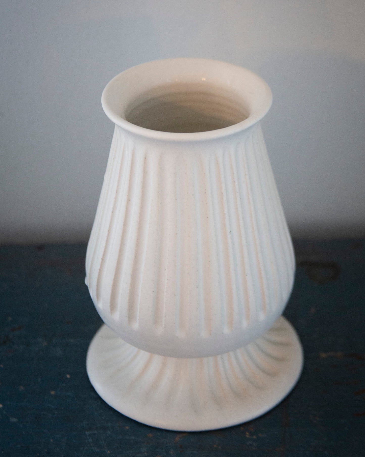 White ribbed vase on a dark surface with a light gray background