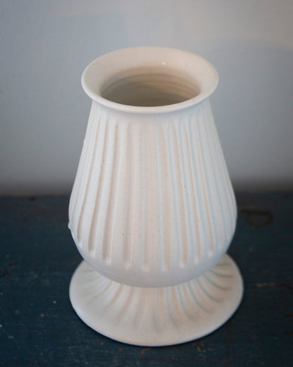 White ribbed vase on a dark surface with a light gray background