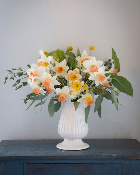 Floral arrangement in a white vase on a wooden surface with a gray background