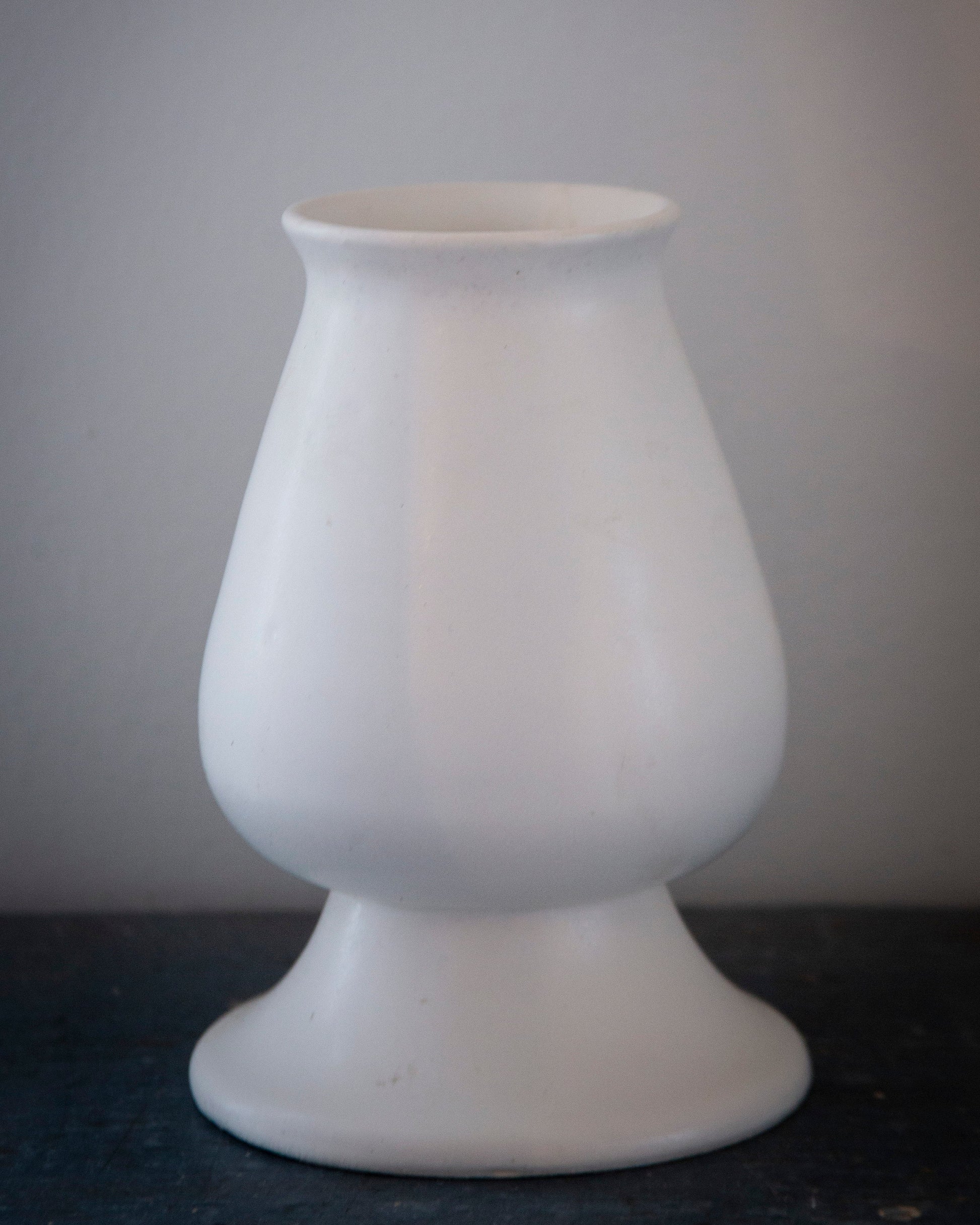 White ceramic vase on a dark surface with a gray background
