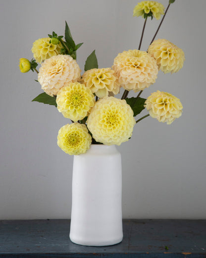 White vase with yellow flowers on a gray surface