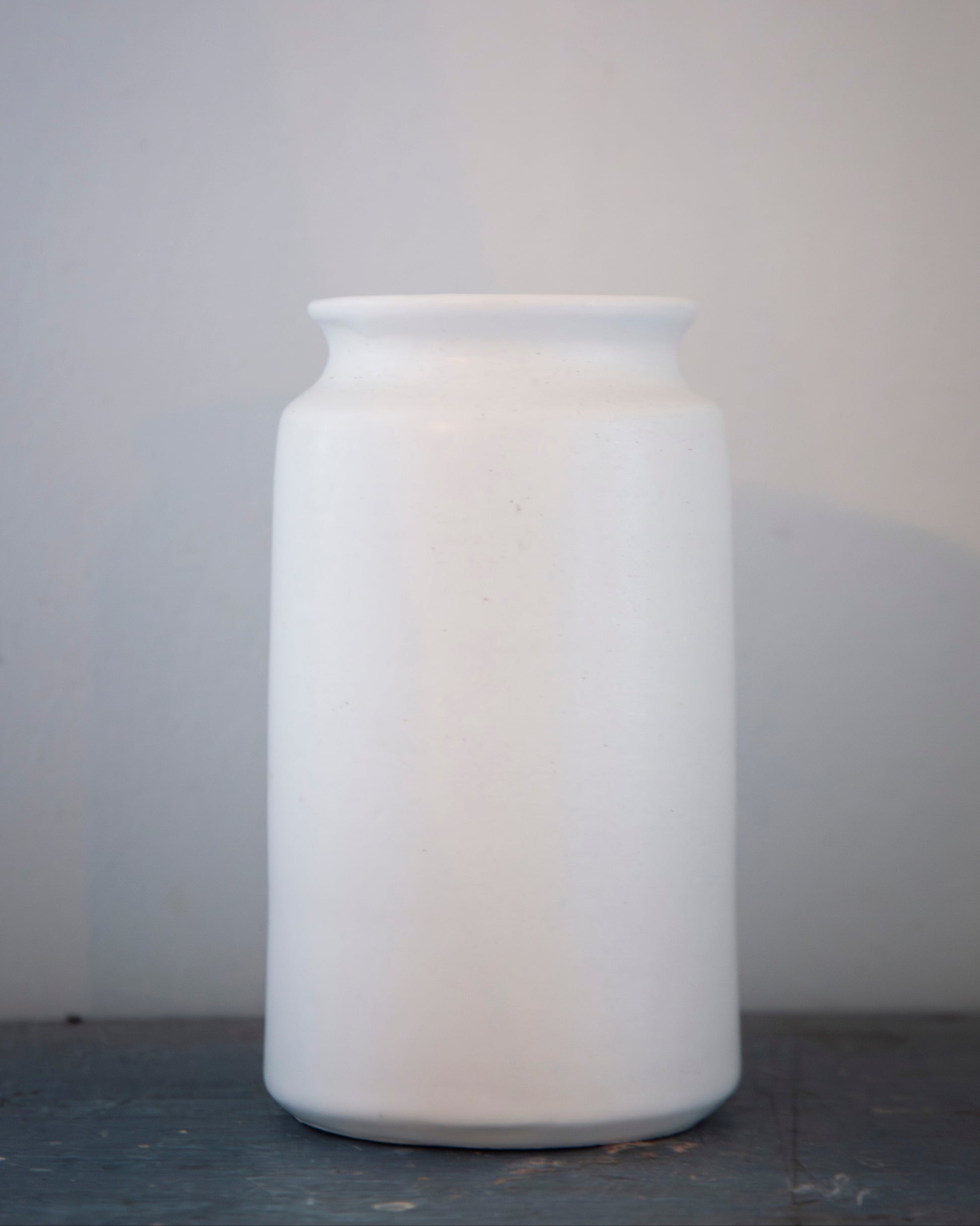 White ceramic jar on a gray surface with a light gray background