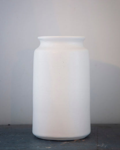 White ceramic jar on a gray surface with a light gray background