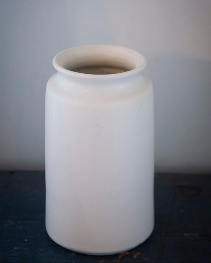 White ceramic vase on a dark surface with a gray background