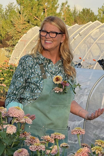 Woman in a green apron standing among flowers and greenery