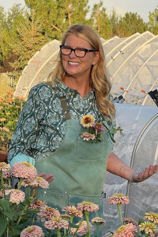 Woman in a green apron standing among flowers and greenery
