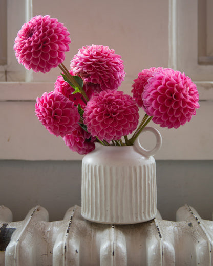 White vase with pink flowers on a radiator against a neutral wall.