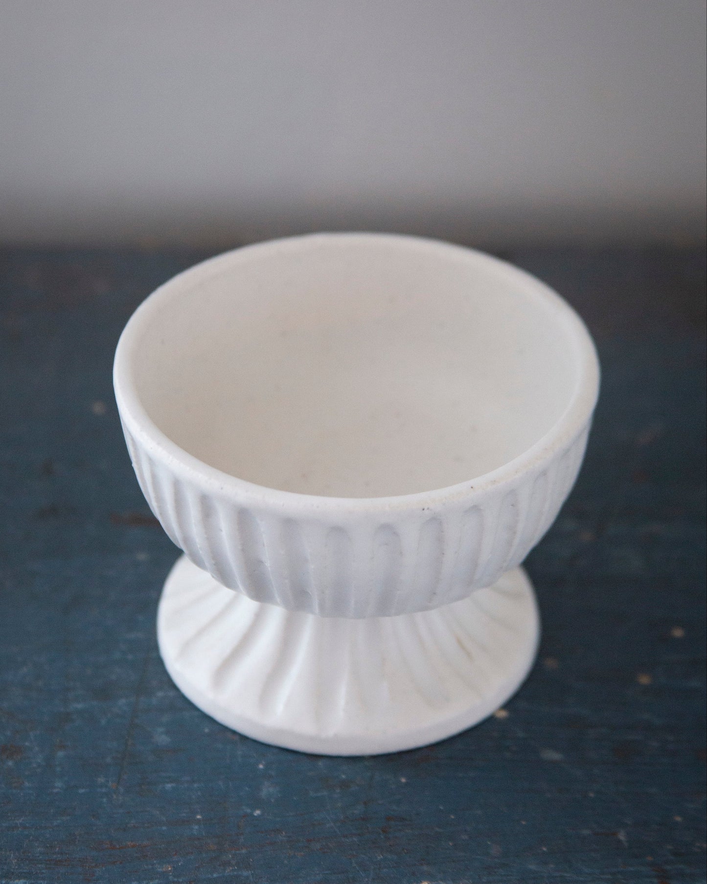 White ceramic footed bowl on a dark surface with a gray background