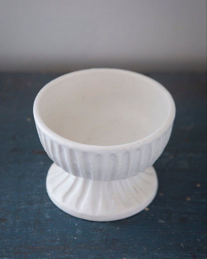 White ceramic footed bowl on a dark surface with a gray background